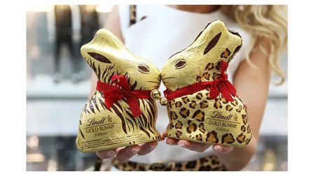 A person holding two Lindt golden bunnies decorated with leopard and zebra prints facing each other. 