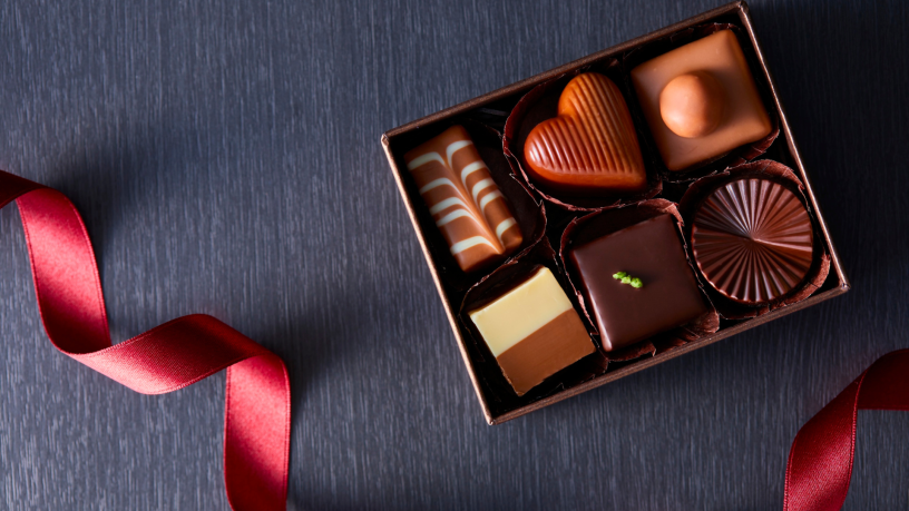 A small box containing six chocolates, next to a red gift ribbon